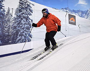 Male skier in orange jacket skiing down a snow slope from right to left