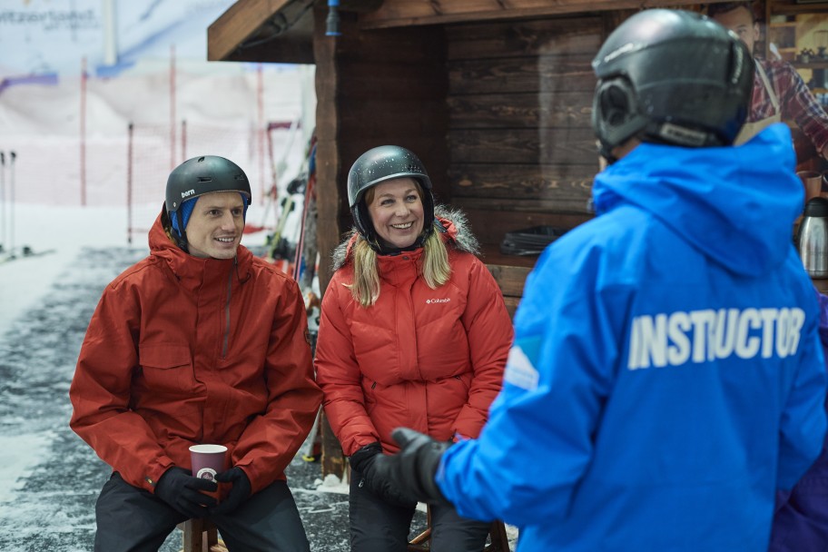 Instructor speaking to a couple in ski gear sat on a bench