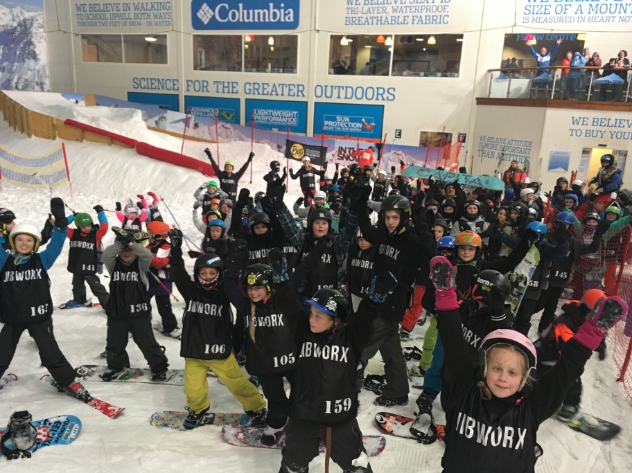 Big group of kids on skis and snowboards posing for photo in an indoor slope near London