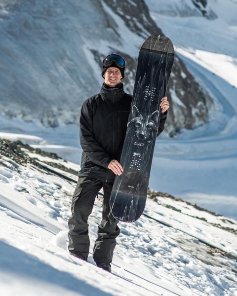 Snowboarder posing with snowboard with snowy mountain background