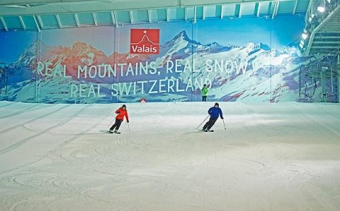 Two people skiing down an indoor slope near London side by side