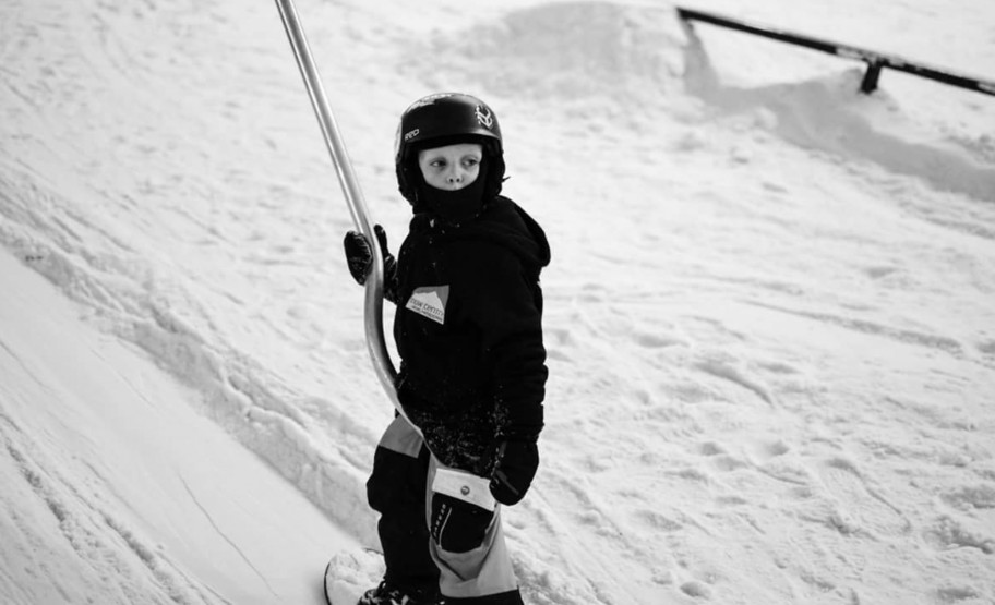 Young child on snowboard going up the slope using a poma lift